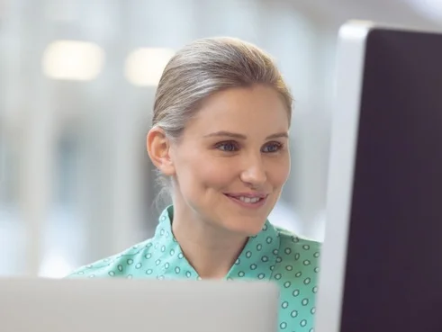 Smilende kvinne som jobber ved en PC på kontoret