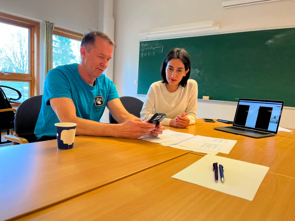 UX-designer Farnaz Shahriari sitter ved et bord og ser på mens en bruker tester en prototype på mobilen