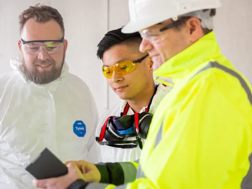 Three workers in protective equipment looking at a tablet