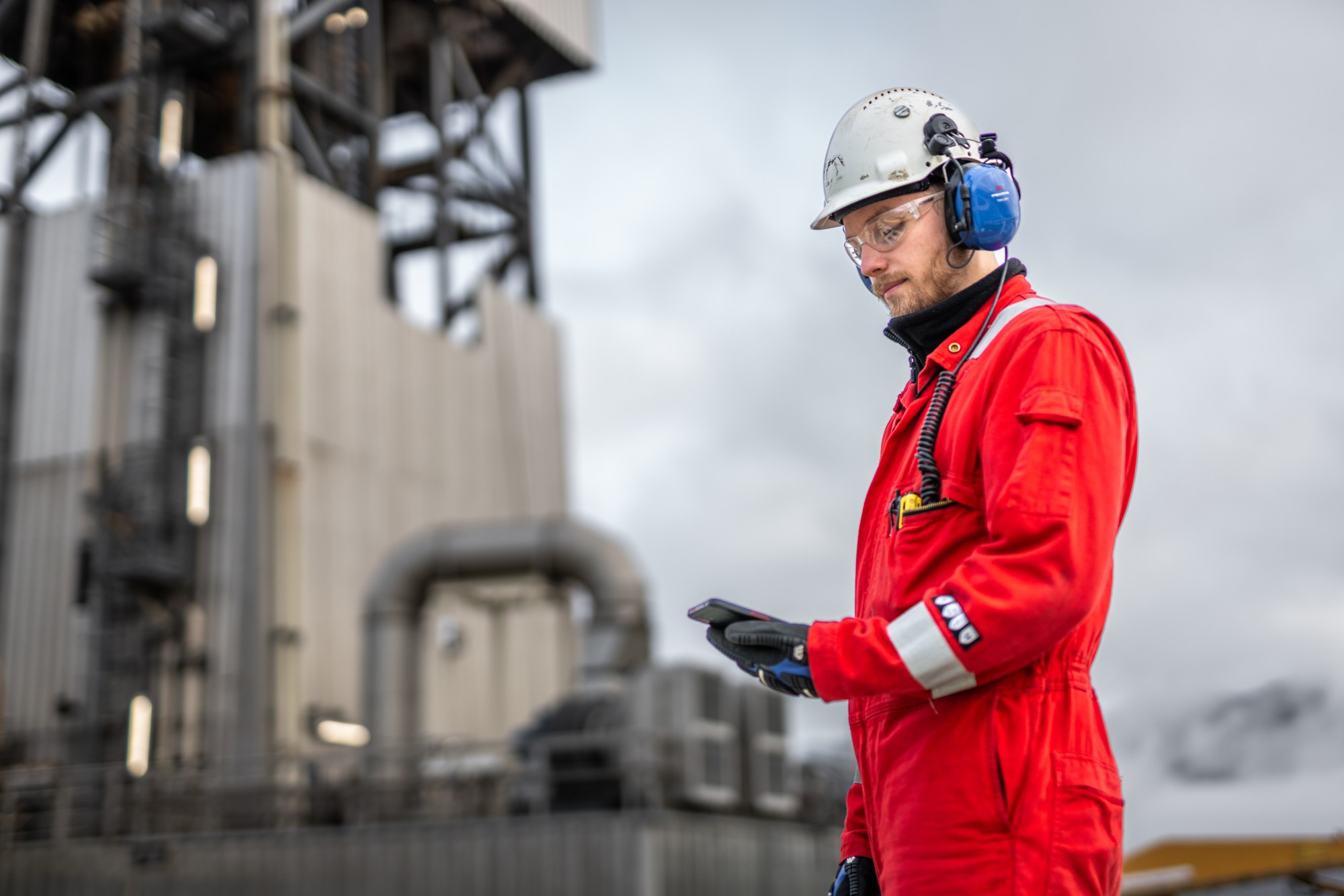Inspector in protective equipment looking at a mobile phone at an industrial site